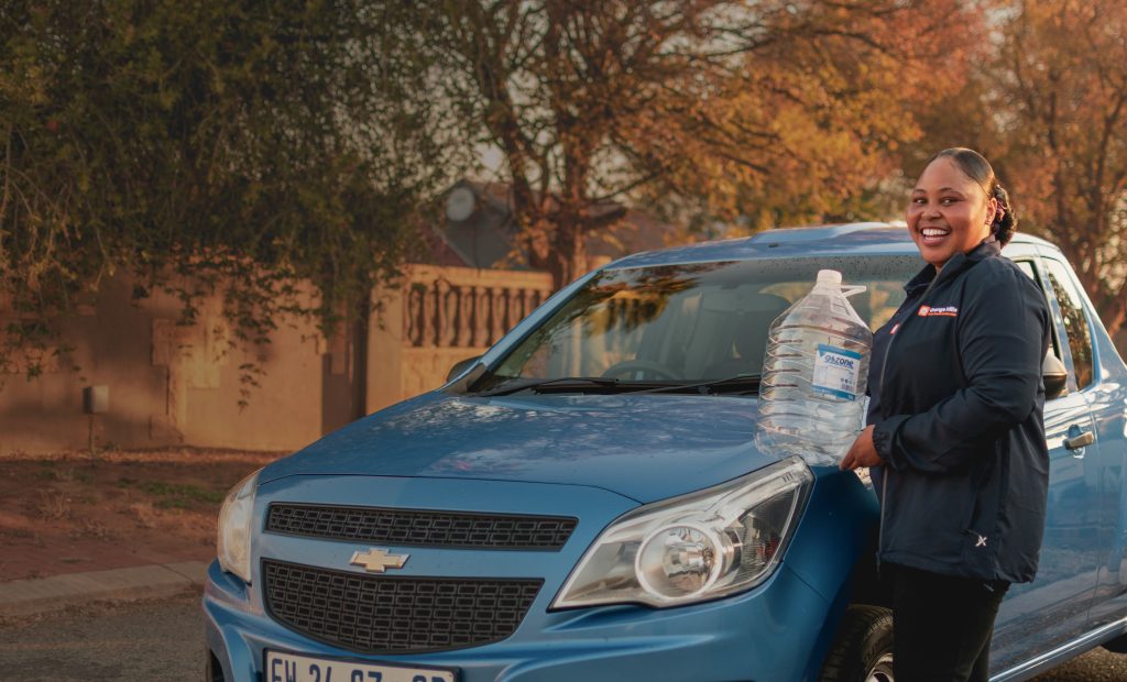 Nthabiseng Mashaba, Orange Hills founder, holding a bottle of water beside the delivery car.